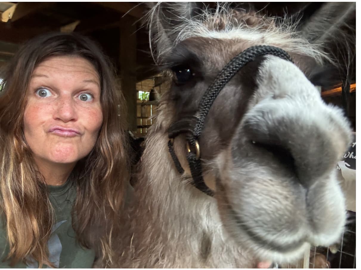 Karine making a silly face next to a llama on her farm